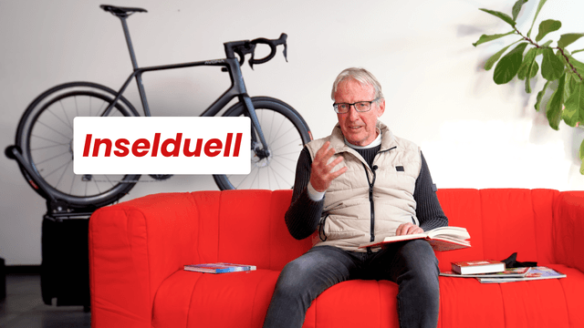 Mann sitzt auf rotem Sofa, Bücher und ein Fahrrad im Hintergrund. Text "Inselduell" auf weißem Feld.
